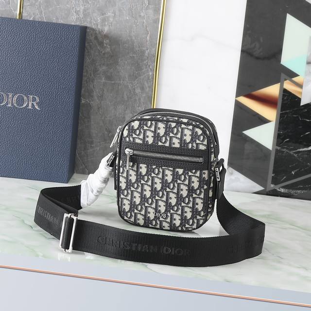 470 Dior 这款信使包是本季新品，精巧实用，是日常的理想良伴。采用米色和黑色 Oblique 印花面料精心制作，饰以黑色粒面牛皮革细节。拉链隔层和正面口袋