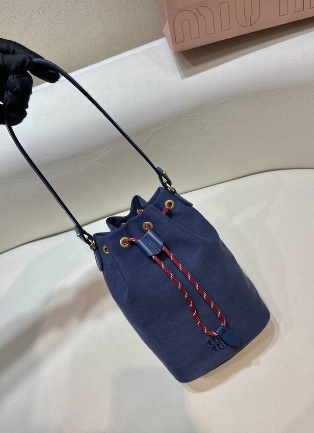 新款水桶包5Nr038 这款水桶包采用华达呢织物与同色系刺绣徽标，赋予了这款小袋百搭特质，双色编织饰带抽绳彰显M永风格本真，编织抽绳开合，皮革手提柄。容量空间大