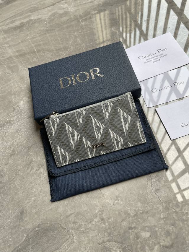 这款拉链卡夹实用而不失优雅。采用迪奥灰Cd Diamond图案帆布精心制作，从Dior档案汲取灵感，饰以同色调光滑牛皮革细节。设有一个带有拉链的角撑式隔层，背面