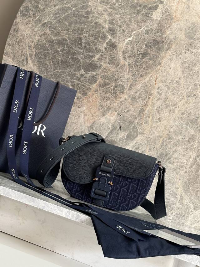 这款马鞍手拿包附有肩带，是二零二五春季男装系列推出的新款单品，采用时尚的设计，彰显精致的优雅气质，为经典的马鞍系列提升格调。采用提花面料精心制作，饰以金属光泽线