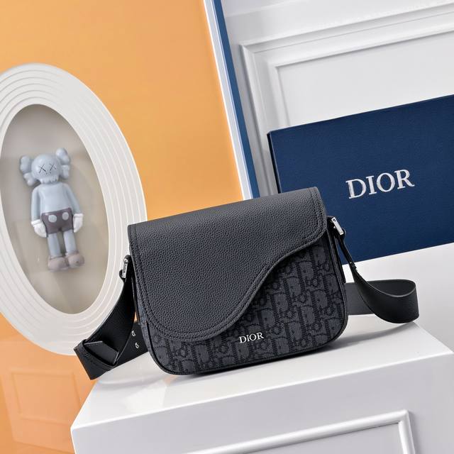 配全套折叠礼盒 Di.Or 迷你马鞍信使包精巧时尚。采用黑色 Oblique 印花面料精心制作，饰以同色调粒面牛皮革翻盖和Logo标志，突显马鞍包的精致魅力。内