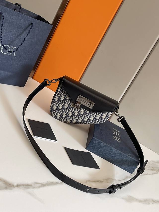 d家这款信使包经典优雅，彰显个性魅力。采用米色和黑色 Oblique 印花面料精心制作。造型硬朗，饰以黑色光滑牛皮革翻盖，搭配金属覆层黄铜扣环开合。内部隔层可收