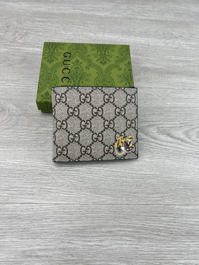 gucci 饰Gg虎印花钱包。Gucci小件皮革配饰突破设计界限，不断以个性方式焕新演绎经典单品。这款男士钱包将经典Gg Supreme帆布与黑色Gg配件匠心糅