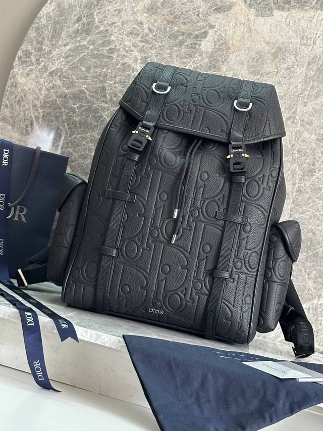 这款 Dior Hit The Road 翻盖双肩背包将现代风格与 Dior 的高订精神融为一体。采用黑色 Oblique 印花面料等材质精心制作，饰以同色调粒