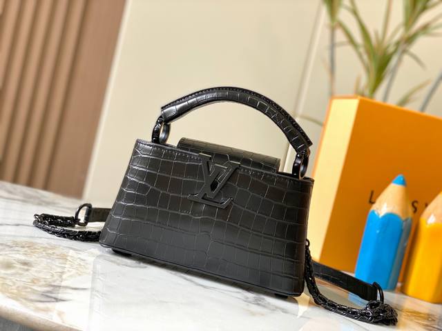 升级版 M23977黑色鳄鱼纹本款Capucines小号手袋为哑光Taurillon牛皮革搭配金属件，令经典设计展露利落风范。翻盖提供外置或内收两式风尚，齐整内