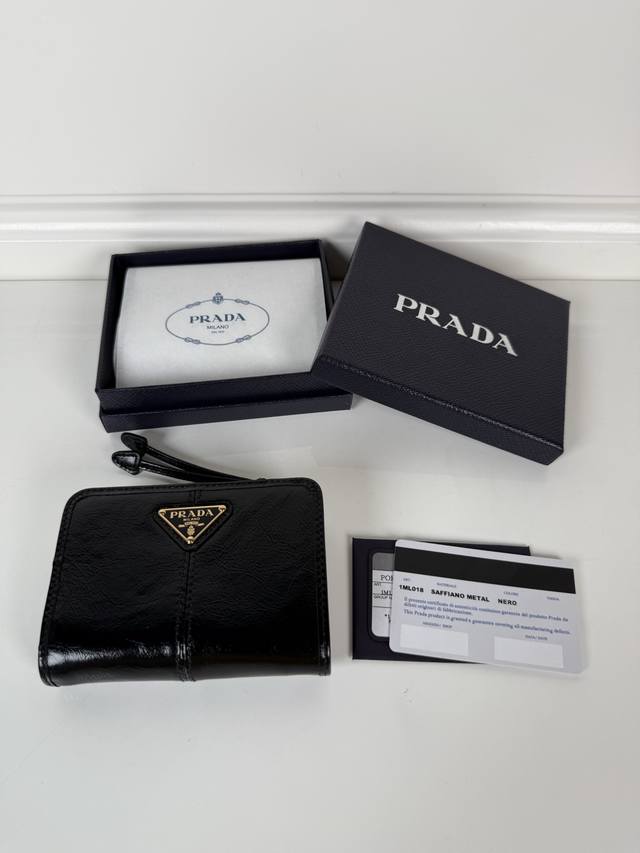 p家黑色油腊牛皮制作短夹，型号1Ml018，按扣开合设计，内设9个卡槽，一个钞票隔层，一个带拉链的零隔层，尺寸12 X 8Cm，尺寸小巧但功能齐全，实用与时尚兼