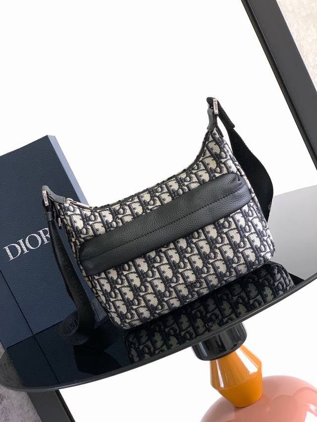 这款 Rider Soft 水饺包是二零二五秋季男装系列新品 兼具实用功能与时尚设计 采用米色和黑色 Oblique 印花面料等材质精心制作 饰以黑色粒面牛皮革