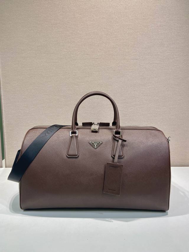 新款旅行包2Vc018新色 这款优雅的旅行袋采用Saffiano皮革制作，配有环绕式拉链和尼龙肩带，彰显严谨的设计理念。并装饰有皮革姓名标牌和带刻字徽标的金属锁