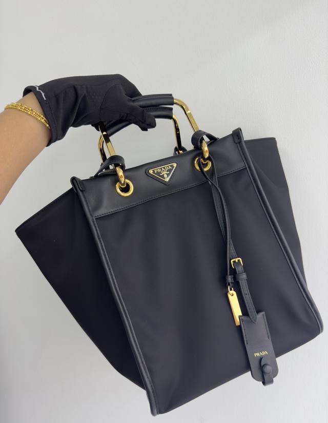 新款托特包1Bg578 这款托特包采用时尚几何造型，融合实用的Re-Nylon再生尼龙材质与精致细节。造型百变，搭配金属与皮革双手提柄，可在手提包与单肩包之间随