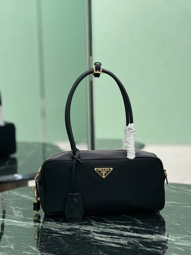 新款锁头包 小号 这款手提包造型挺括而小巧，采用再生尼龙 Re-Nylon 和皮革材质，精致优雅。饰有金属五金配件和涂珐琅三角形金属徽标，拉链和挂锁开合增添别致