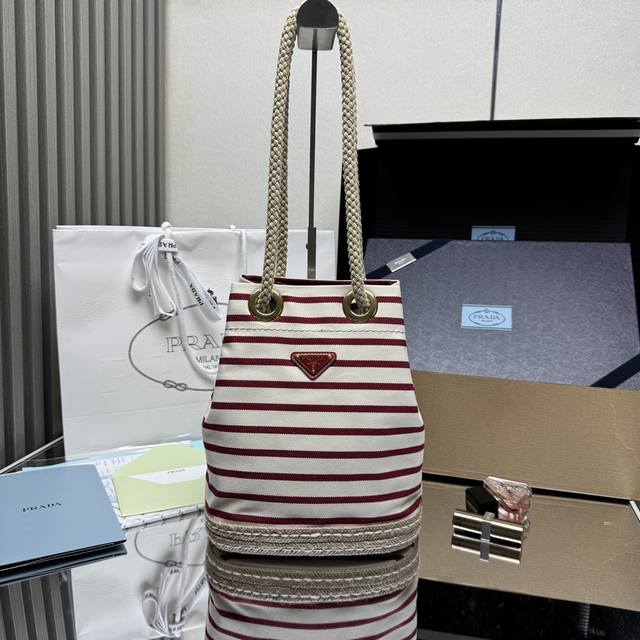 顶级原单 新款水桶包1Be082条纹款这款织物水桶包饰以航海风条纹图案，为造型增添色彩。底部的设计灵感源自草编鞋，绳索则是象征着航海世界的另一细节元素，共同营造