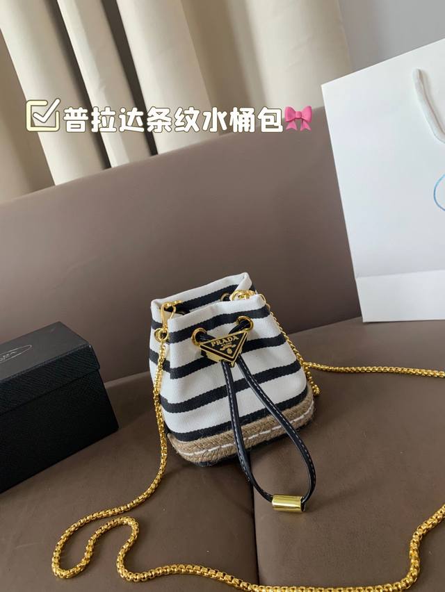 普拉达新款条纹水桶包 这款迷你小包崭新诠释经典航海风元素，呈现典雅的夏日质感与精致细节。选用条纹织物打造，底部的设计灵感源自草编鞋，搭配皮革抽绳与精致可拆卸肩带