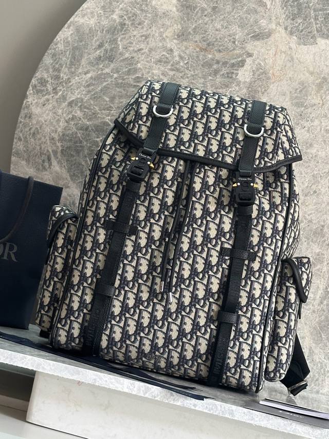 正品级 ，高版本 这款 Dior Hit The Road 翻盖双肩背包将现代风格与 Dior 的高订精神融为一体。采用黑色 Oblique 印花面料等材质精心