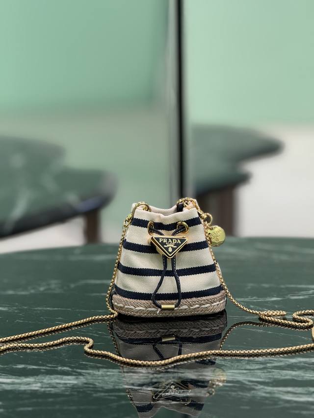 迷你小水桶 这款迷你小包崭新诠释经典航海风元素，呈现典雅的夏日质感与精致细节。选用条纹织物打造，底部的设计灵感源自草编鞋，搭配皮革抽绳与精致可拆卸肩带。 尺寸：