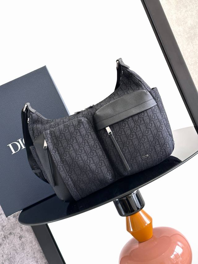 这款 Rider Soft 水饺包是二零二五秋季男装系列新品，兼具实用功能与时尚设计。采用黑色 Oblique 印花面料精心制作，饰以同色调粒面牛皮革细节和 D