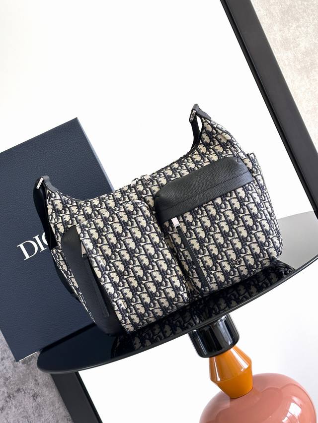 这款 Rider Soft 水饺包是二零二五秋季男装系列新品，兼具实用功能与时尚设计。采用米色和黑色 Oblique 印花面料精心制作，饰以黑色粒面牛皮革细节提