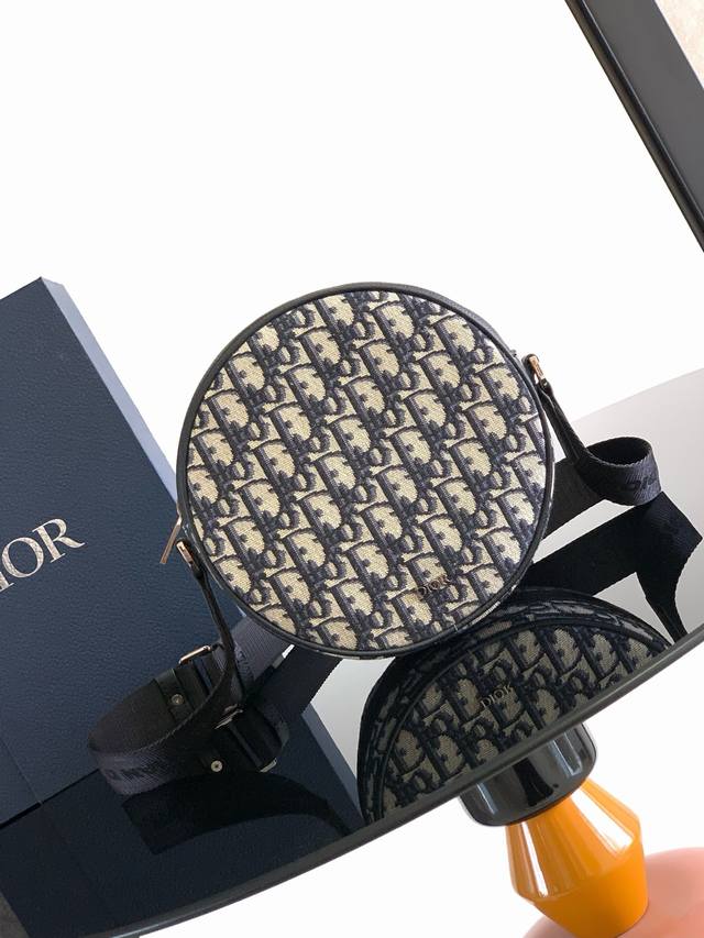 这款 Dior Yoyo 拉链信使包时尚实用。圆形款式，采用米色和黑色 Oblique 印花面料等材质精心制作，饰以黑色粒面牛皮革细节提升格调，正面点缀以 Di
