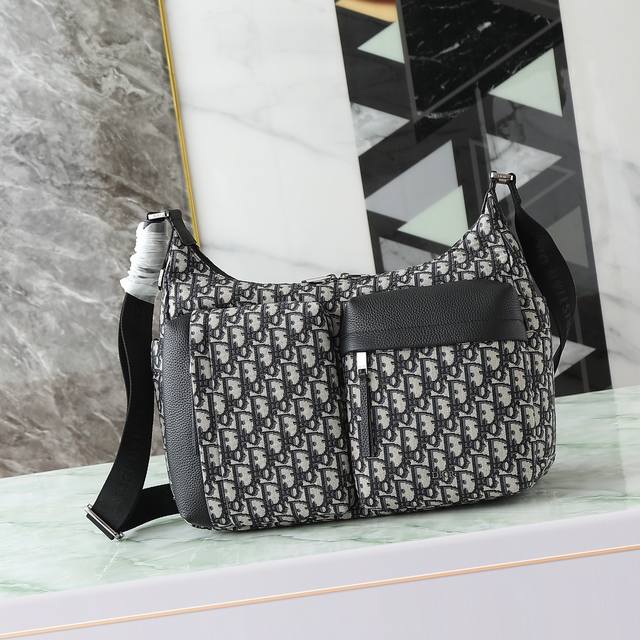 这款 Rider Soft 水饺包是二零二五秋季男装系列新品，兼具实用功能与时尚设计。采用米色和黑色 Oblique 印花面料精心制作，饰以黑色粒面牛皮革细节提