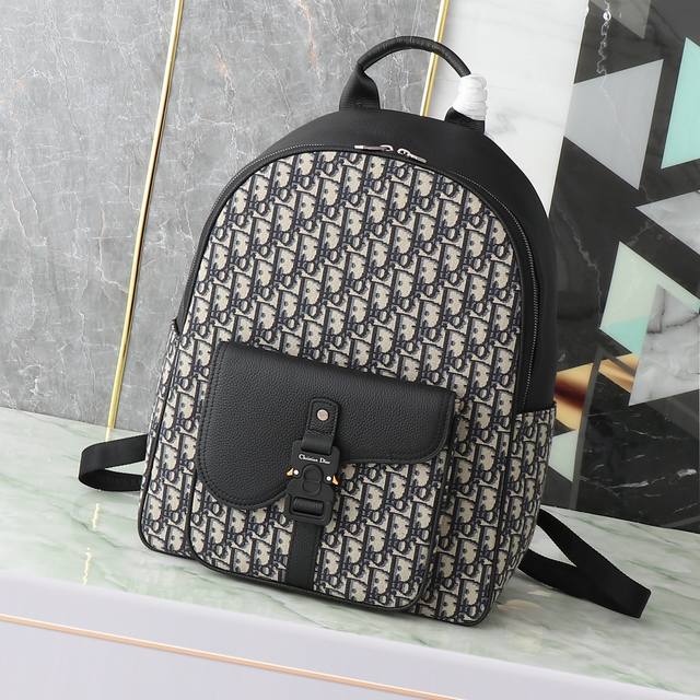 这款马鞍拉链双肩背包是二零二四冬季男装系列新品，采用时尚的原创设计，突显马鞍风格。采用米色和黑色 Oblique 印花面料精心制作，饰以黑色粒面牛皮革细节。空间