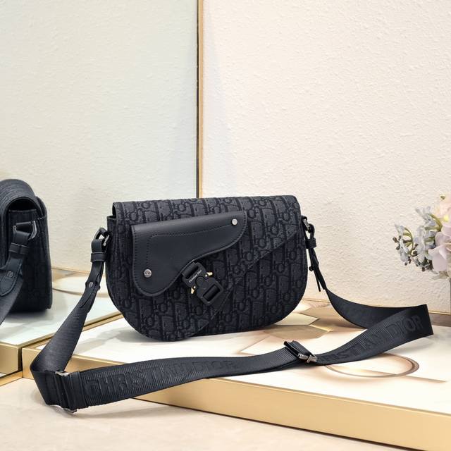 迪奥Dior单肩马鞍信使包 黑布]型号 1030 这款马鞍信使包是二零二四秋季男装系列新品，精巧时尚。采用黑色 Oblique 印花面料精心制作，正面饰以一个贴