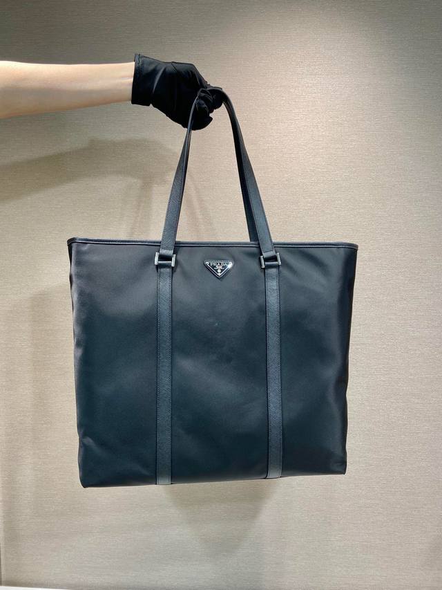 新款托特包2Vg112 这款托特包取材Re-Nylon再生尼龙打造，饰以Saffiano皮革细节，扁平皮革提手，正面涂珐琅金属三角形徽标，内部配拉链式口袋，容量