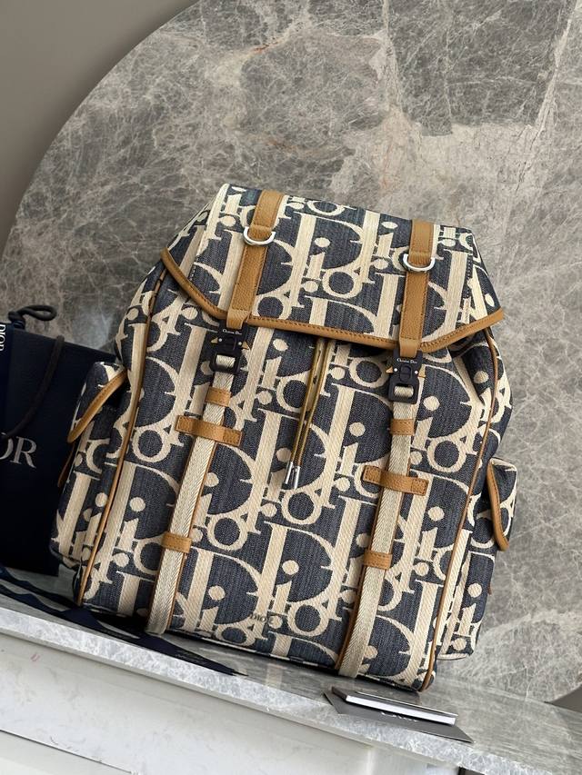 正品级 这款 Dior Hit The Road 翻盖双肩背包将现代风格与 Dior 的高订精神融为一体。采用酒椰草效果 Oblique 印花牛仔面料等材质精心