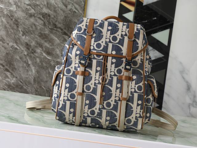 这款 Dior Hit The Road 翻盖双肩背包将现代风格与 Dior 的高订精神融为一体。采用酒椰草效果 Oblique 印花牛仔面料等材质精心制作，饰