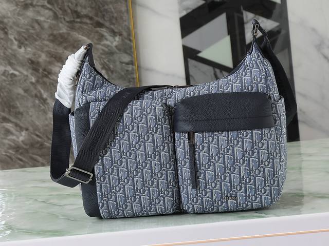 这款Rider Soft水饺包是二零二五秋季男装系列新品，兼具实用功能与时尚设计。采用蓝色Oblique 印花面料等材质精心制作，饰以同色调粒面牛皮革细节和Di