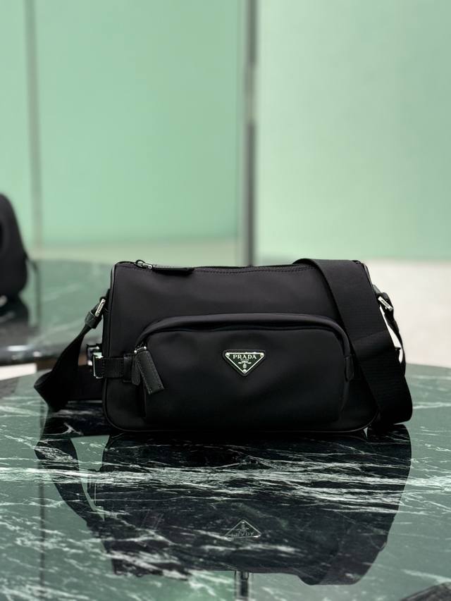 新款邮差包 小号 这款单肩包的运动功能性由简约线条和实用现代细节定义。包身采用创新性的Re-Nylon再生尼龙材质打造，搭配Saffiano牛皮革细节，增添独特