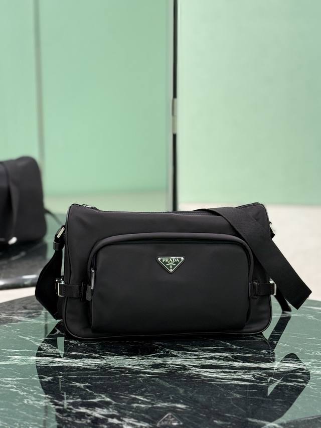 新款邮差包 大号 这款单肩包的运动功能性由简约线条和实用现代细节定义。包身采用创新性的Re-Nylon再生尼龙材质打造，搭配Saffiano牛皮革细节，增添独特