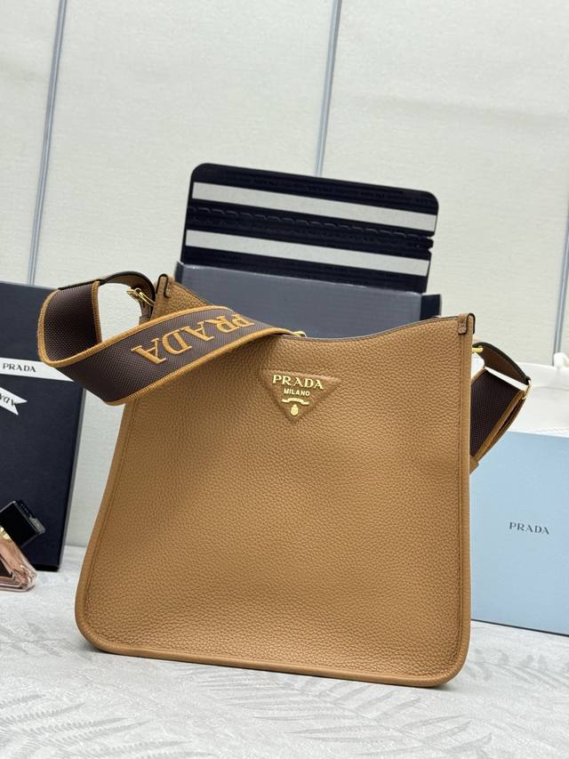 新款织物斜跨包1Bc073 大号焦糖金扣Tote包 这款皮革迷你单肩包设计简约。正面金属三角形徽标平添标志性格调。配有可拆卸 调节徽标印花织带，上身效果非常美彰