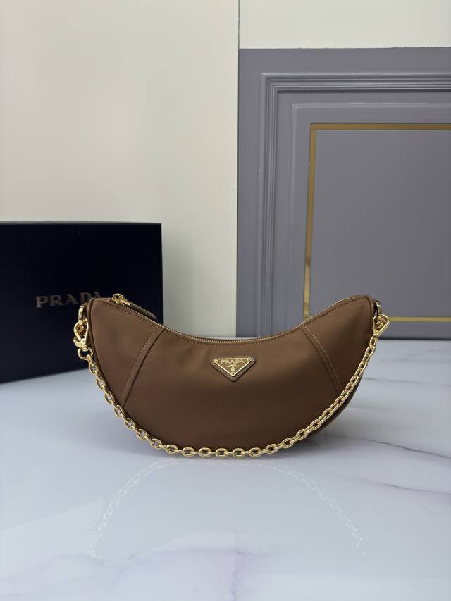 新品月牙包1Bh222多功能 这款Re-Nylon手袋采用再生尼龙面料制作，精致而百搭，融合档案库造型与实用的当代风格。半月廓形，搭配可拆卸运动风肩带与优雅的链