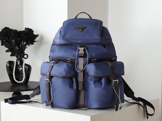 新品牛皮革拼接双肩背包2Vz117此款双肩背包融合精致与实用功能，呈现柔和线条的混搭廓形，设计的二元性通过轻盈实用的Re-Nylon再生尼龙与经典风格的结合得以