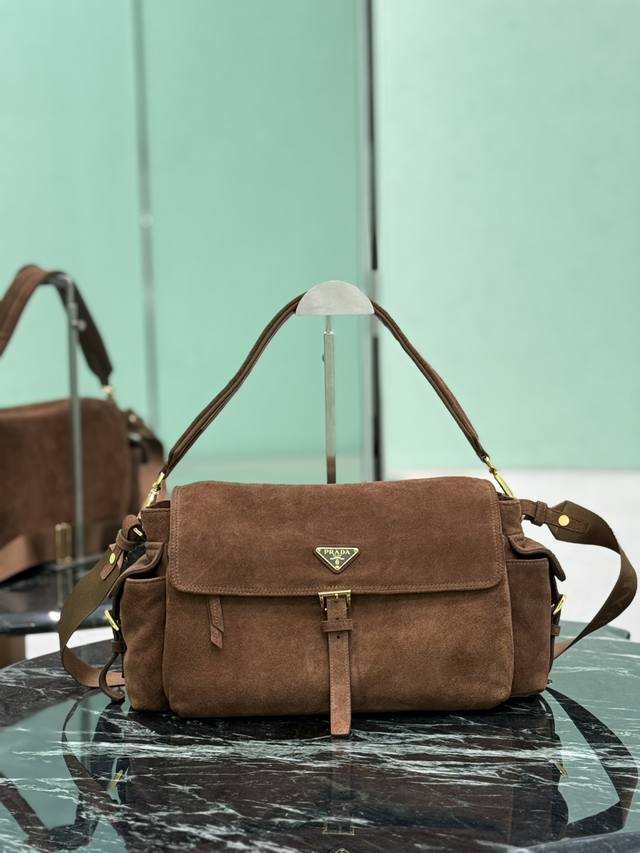 新款邮差包 大号 这款手袋完美融合精致与功能性，采用进口麂皮轮廓柔和，配有多个口袋。轻盈实用的设计结合运动与百搭元素，饰有涂珐琅三角形金属徽标，搭配皮革细节。配