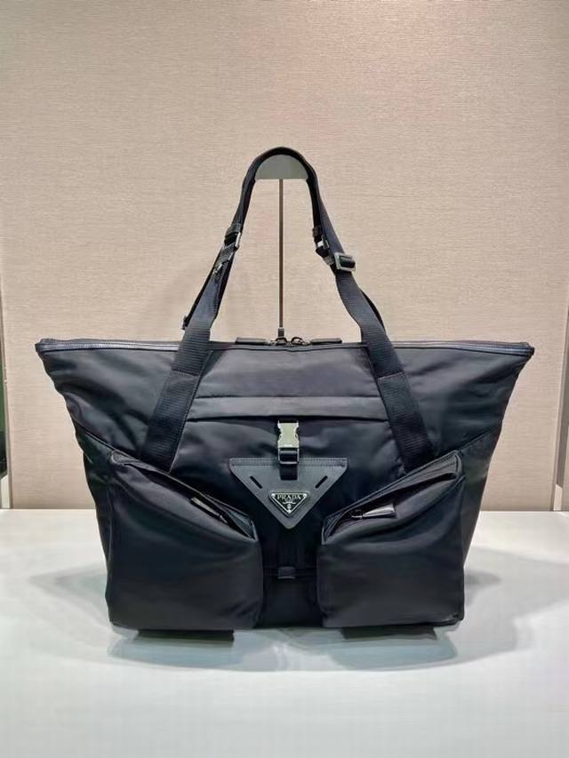 新款旅行包2Vc040 DDD 这款旅行包采用进口尼龙面料。容量充裕，配有可调式提手，设有大号工装侧袋与中袋，配有侧插扣，点缀标志性的涂珐琅三角形金属徽标。搭配