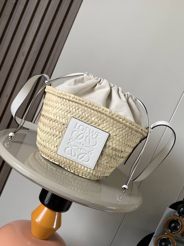 棕榈叶和牛皮革抽绳水桶包 这款水桶包的经典包身采用棕榈叶手工编织而成配有一根牛皮革肩带和人字纹棉质帆布抽绳顶部此手袋在西班牙采用由摩洛哥工匠种植、收成、晒干和手