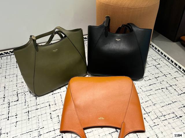 Prada 普拉达这款皮革托特包采用进口小牛，内配进口羊皮，既充满精致魅力，又富有实用性。搭配可调节皮革提手，饰有经典设计的金属扣环，呈现出时尚而现代的细节s。