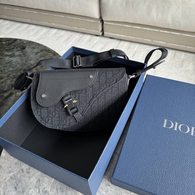 马鞍信使包 325 这款马鞍信使包是二零二四秋季男装系列新品，精巧时尚。采用oblique 印花面料精心制作，饰以同色调粒面牛皮革马鞍翻盖，搭配铝扣提升格调。宽