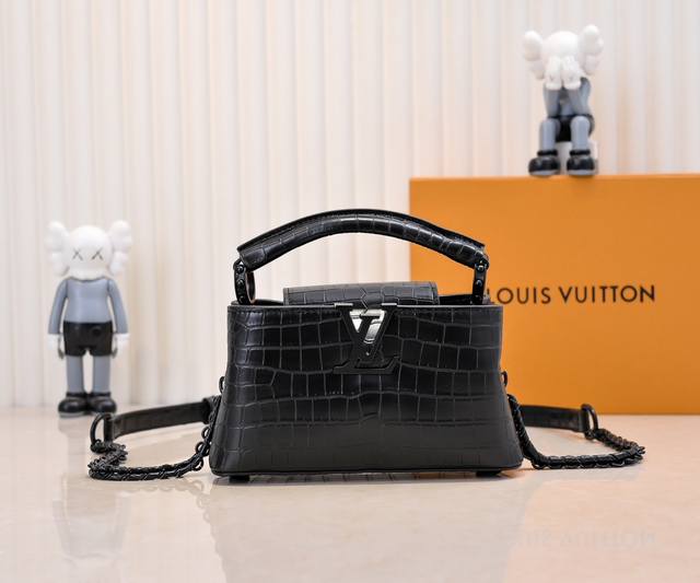 升级版 M23977黑色鳄鱼纹本款Capucines小号手袋为哑光Taurillon牛皮革搭配金属件，令经典设计展露利落风范。翻盖提供外置或内收两式风尚，齐整内