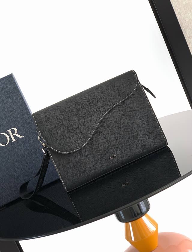 A5 三角手拿包是 Dior 的全新主打单品。采用黑色粒面皮革等材质精心制作，搭配马鞍廓形翻盖，宽敞的拉链隔层可收纳手机，另外还设有卡槽。搭配可拆卸的腕带，便于
