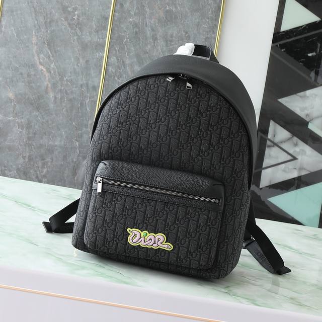 Rider 2.0 拉链双肩背包来自 Dior And Kaws 限定系列。采用黑色粒面牛皮革等材质精心制作,正面大号拉链口袋饰以同色调 Oblique 印花, Rider 2.0 拉链双肩背包来自 Dior And Kaws 限定系列。采用黑色粒面牛皮革等材质精心制作,正面大号拉链口袋饰以同色调 Oblique 印花,