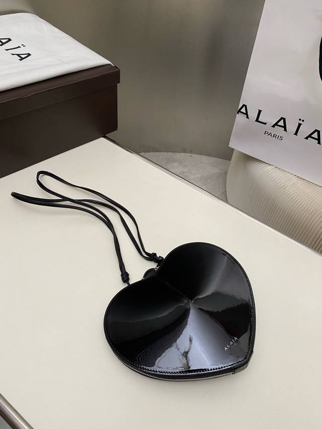 Alaia爱心包雕塑抛光小牛皮肩包。 可调节肩带采用打结设计正面印有徽标双向拉链封口 抛光皮衬里 H7.25英寸X宽8英寸Xd2英寸 供应商颜色：黑色 小牛皮。